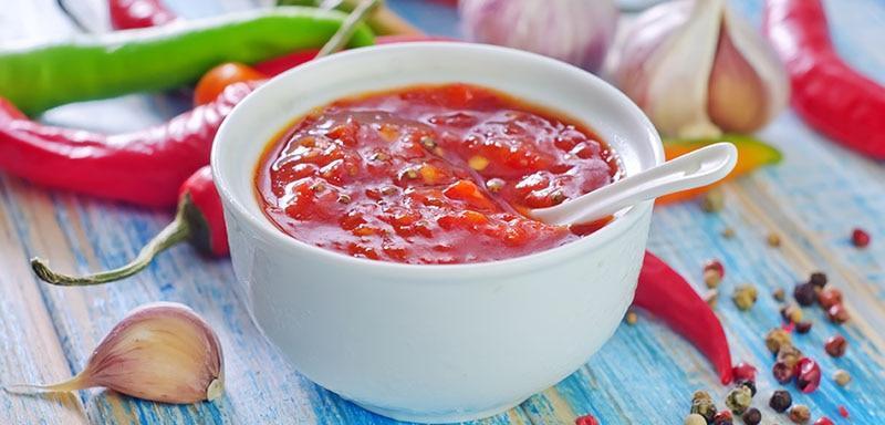 Bowl of chili hot sauce with raw green peppers, red peppers, garlic and peppercorn