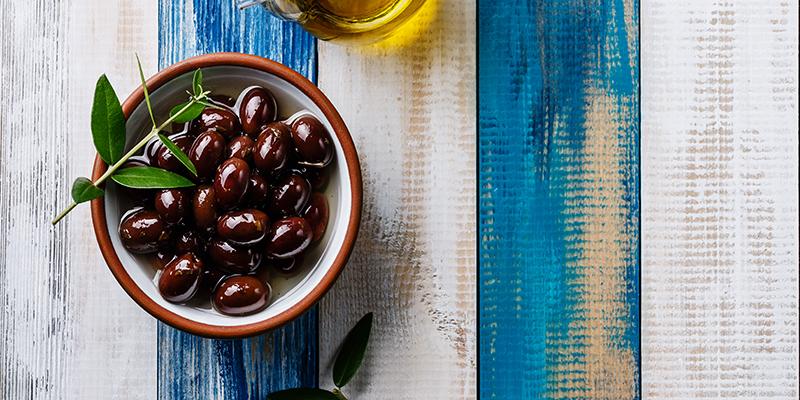 Bowl of Kalamata Olives on blue and white table with olive oil