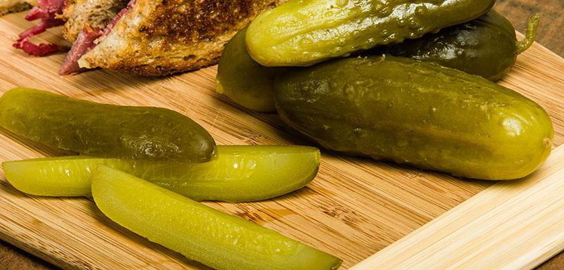 Sliced pickles and whole pickles on a cutting board with a reuben sandwich