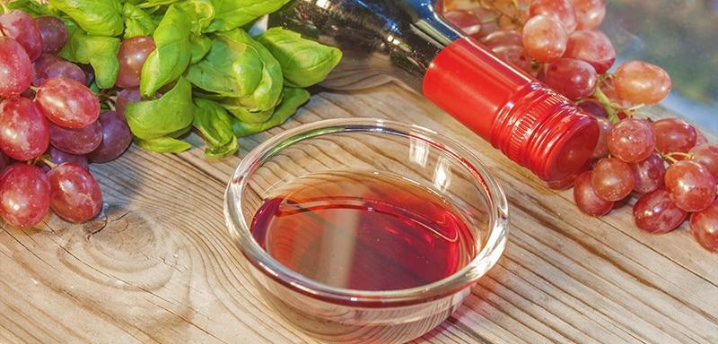 Bowl of red wine vinegar next to a bottle of red wine and grapes